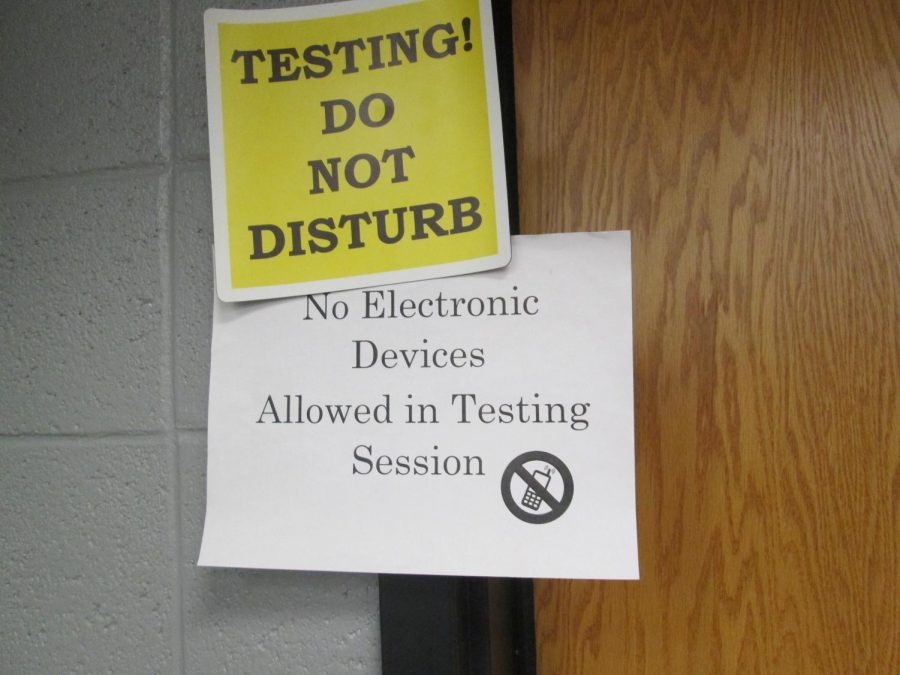 The purpose of the photo is to depict the testing room and the signs that are scattered around the schools as the event is going on. The color resembles caution, and the bold print signifies that there will be consequences if the rules are not followed adequately.