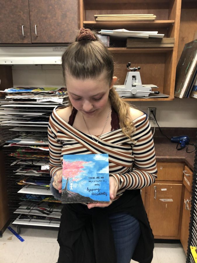 NAHS secretary Alexa Edwards proudly holds her finished Imagination Square. Painted on the square is Bob Ross’ most famous quote: “No mistakes, only happy accidents.” 
